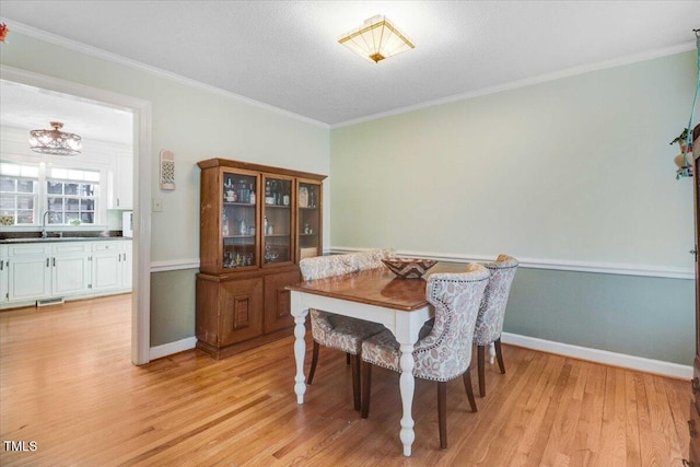 dining space with baseboards, crown molding, light wood finished floors, and an inviting chandelier