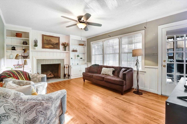 living area with light wood-type flooring, crown molding, built in shelves, and a textured ceiling