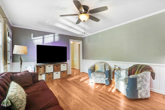 living area featuring wainscoting, wood finished floors, a ceiling fan, and crown molding