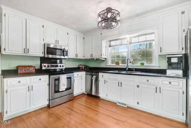 kitchen featuring stainless steel appliances, dark countertops, a sink, and light wood-style floors