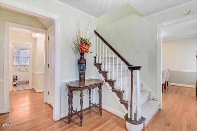 staircase featuring a textured ceiling, ornamental molding, wood finished floors, and baseboards