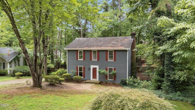 colonial-style house featuring a chimney and a front lawn