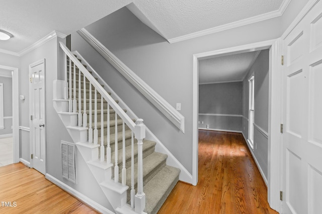 staircase with crown molding, a textured ceiling, visible vents, and wood finished floors