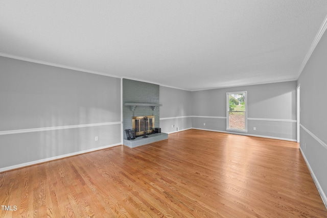 unfurnished living room featuring baseboards, light wood-type flooring, a fireplace, and crown molding