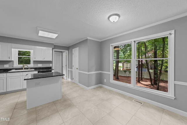 kitchen with crown molding, white cabinetry, a sink, and a center island