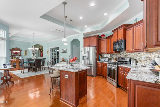 kitchen with a raised ceiling, decorative backsplash, appliances with stainless steel finishes, a sink, and a kitchen bar