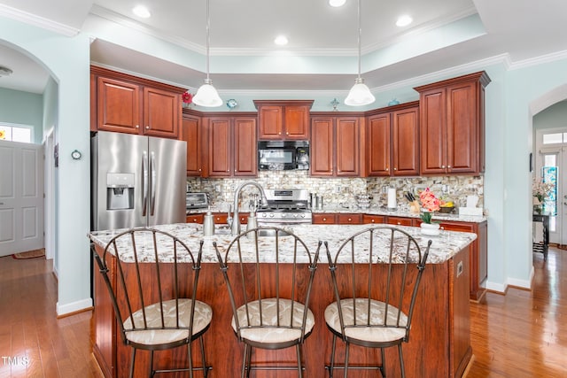 kitchen featuring appliances with stainless steel finishes, arched walkways, a raised ceiling, and pendant lighting