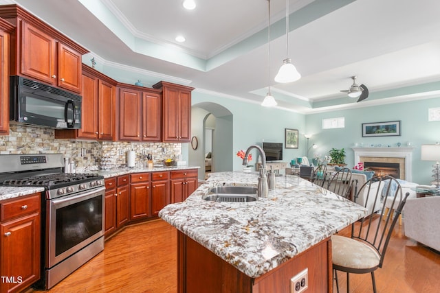 kitchen featuring a raised ceiling, stainless steel range with gas stovetop, open floor plan, black microwave, and a sink