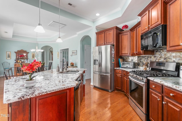 kitchen featuring light wood finished floors, arched walkways, a raised ceiling, stainless steel appliances, and a sink