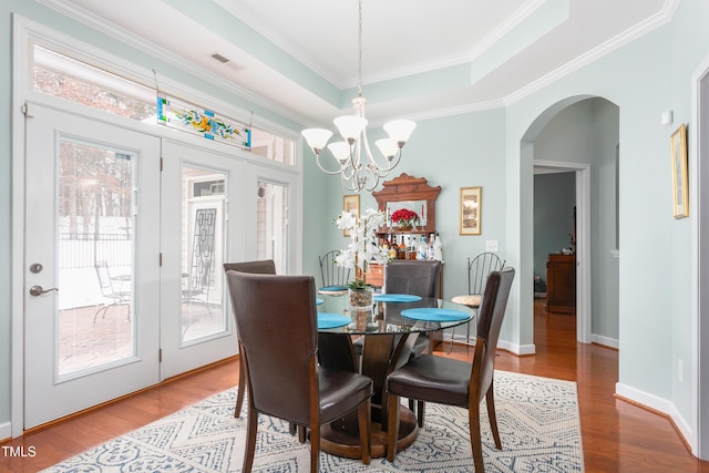 dining area with arched walkways, wood finished floors, baseboards, ornamental molding, and a tray ceiling