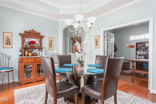 dining area with an inviting chandelier, light wood-style flooring, arched walkways, and crown molding