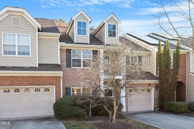 multi unit property with driveway, roof mounted solar panels, a shingled roof, a garage, and brick siding