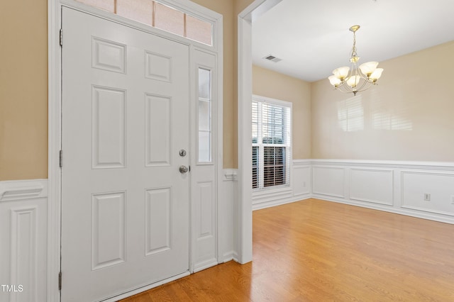 entrance foyer with visible vents, light wood-style flooring, an inviting chandelier, and a wainscoted wall