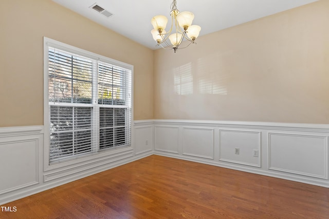 empty room featuring visible vents, a wainscoted wall, an inviting chandelier, and wood finished floors