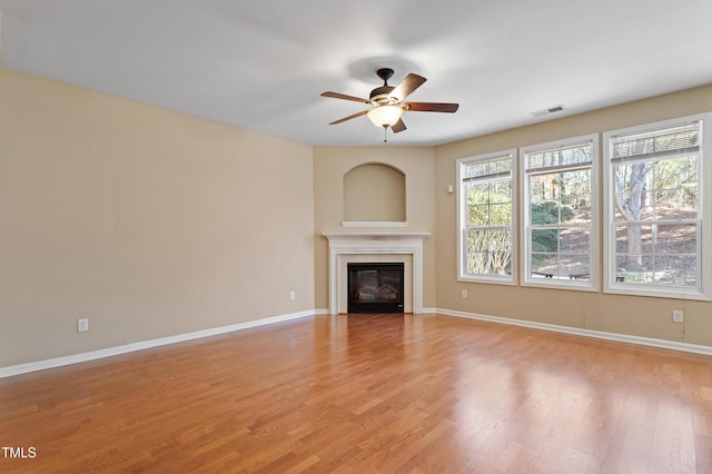 unfurnished living room featuring visible vents, light wood-type flooring, baseboards, and a glass covered fireplace