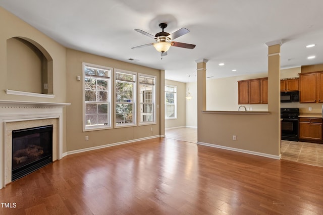 unfurnished living room featuring decorative columns, wood finished floors, visible vents, and baseboards