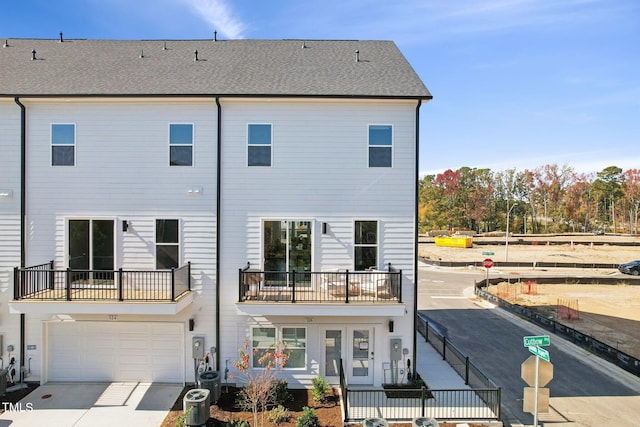 rear view of house with a balcony, a garage, concrete driveway, and roof with shingles