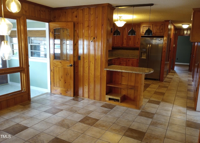 kitchen with light tile patterned floors, a peninsula, stainless steel refrigerator with ice dispenser, brown cabinets, and pendant lighting