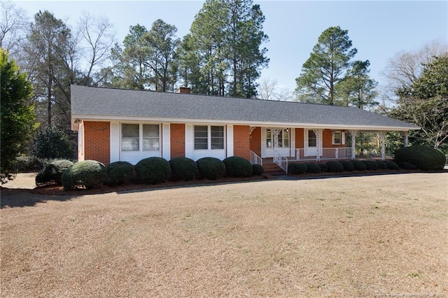 ranch-style house with brick siding, a shingled roof, a chimney, a porch, and a front yard