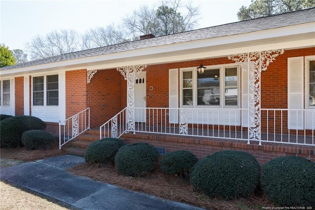 doorway to property with a shingled roof, covered porch, brick siding, and crawl space