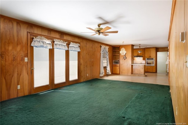 unfurnished living room with wood walls, ceiling fan, and carpet flooring