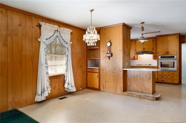 kitchen with wooden walls, visible vents, brown cabinetry, oven, and under cabinet range hood