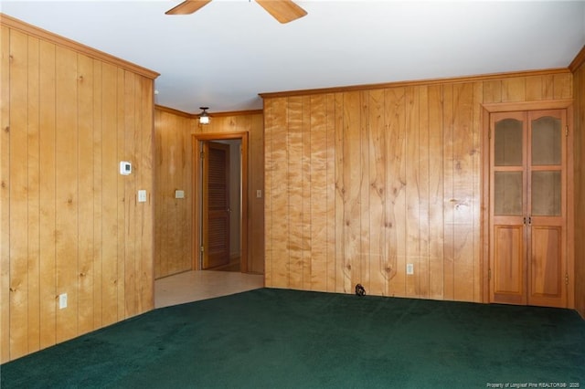 carpeted spare room featuring ceiling fan, ornamental molding, and wooden walls