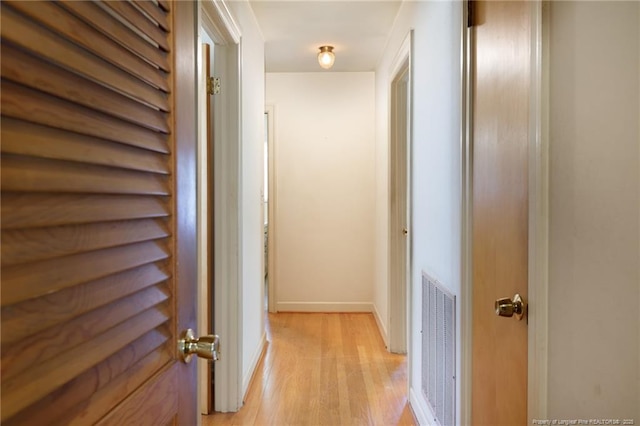 corridor with light wood-style flooring, visible vents, and baseboards