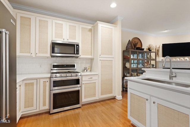 kitchen with light countertops, appliances with stainless steel finishes, ornamental molding, a sink, and light wood-type flooring