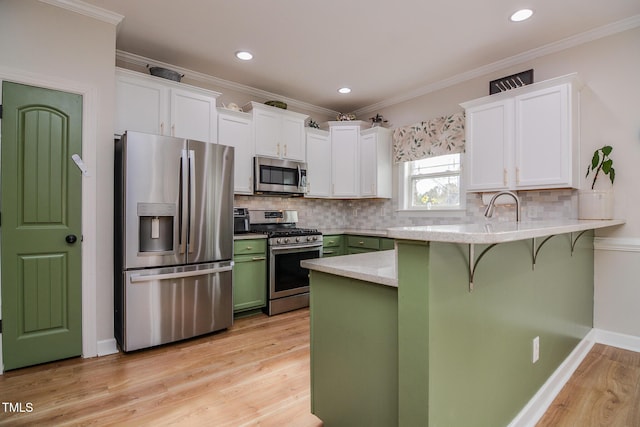 kitchen with white cabinets, a breakfast bar area, a peninsula, stainless steel appliances, and green cabinets