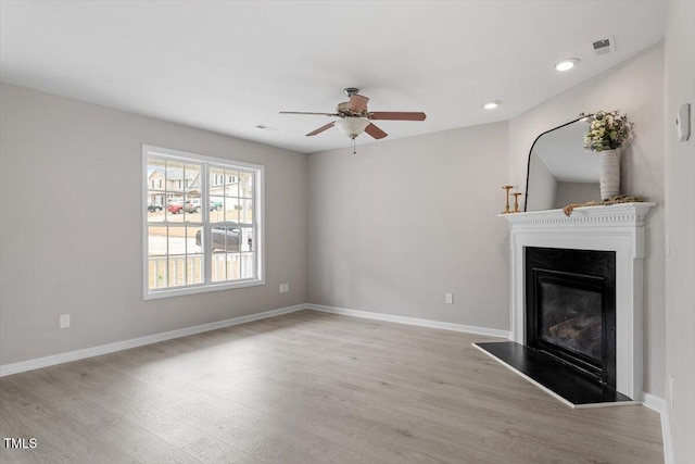 unfurnished living room with visible vents, baseboards, wood finished floors, a glass covered fireplace, and a ceiling fan