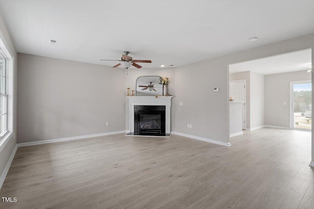 unfurnished living room featuring visible vents, a glass covered fireplace, light wood finished floors, baseboards, and ceiling fan