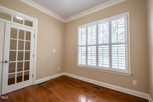 empty room with ornamental molding, wood-type flooring, visible vents, and baseboards