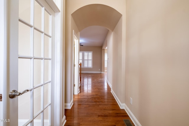 corridor with arched walkways, wood finished floors, visible vents, and baseboards