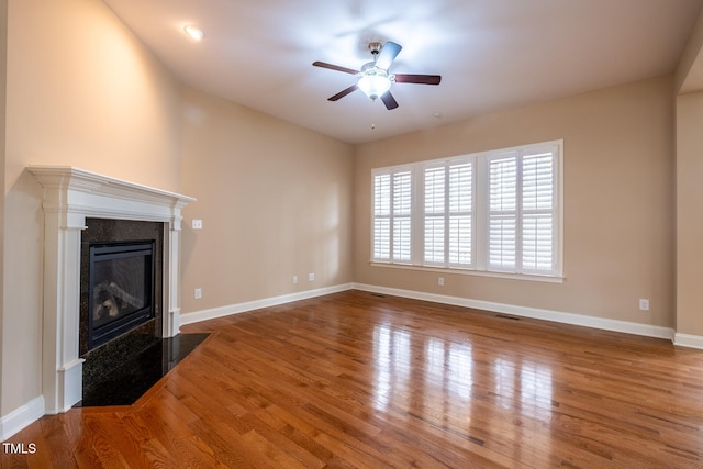 unfurnished living room featuring visible vents, a high end fireplace, ceiling fan, wood finished floors, and baseboards