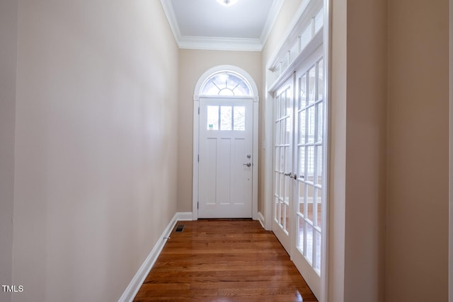 doorway featuring visible vents, crown molding, baseboards, and wood finished floors