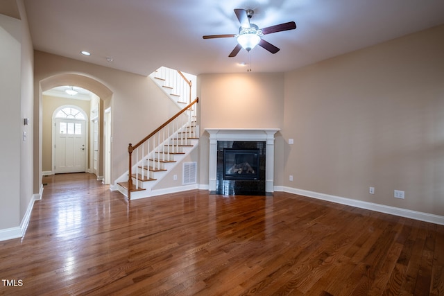 unfurnished living room featuring baseboards, visible vents, arched walkways, stairway, and wood finished floors