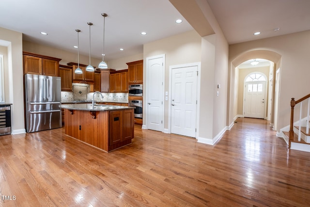 kitchen with a sink, light wood-type flooring, freestanding refrigerator, decorative backsplash, and brown cabinetry