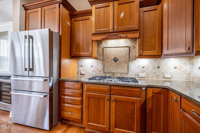 kitchen with appliances with stainless steel finishes, beverage cooler, brown cabinetry, and dark stone countertops