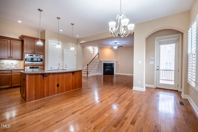 kitchen featuring visible vents, light wood-style flooring, decorative backsplash, brown cabinetry, and a glass covered fireplace