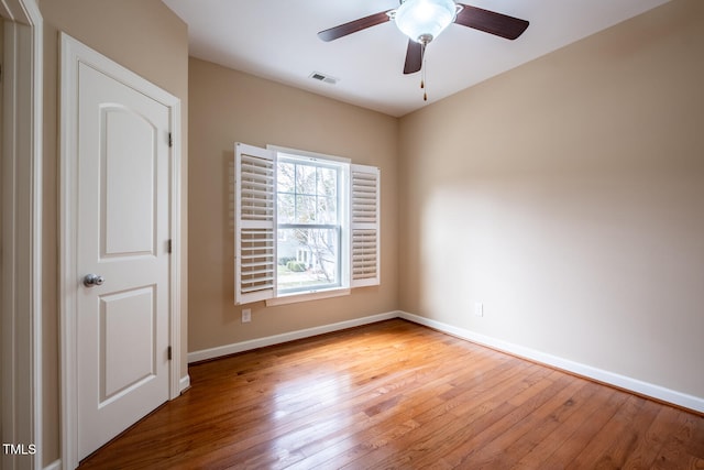 spare room featuring wood-type flooring, visible vents, ceiling fan, and baseboards