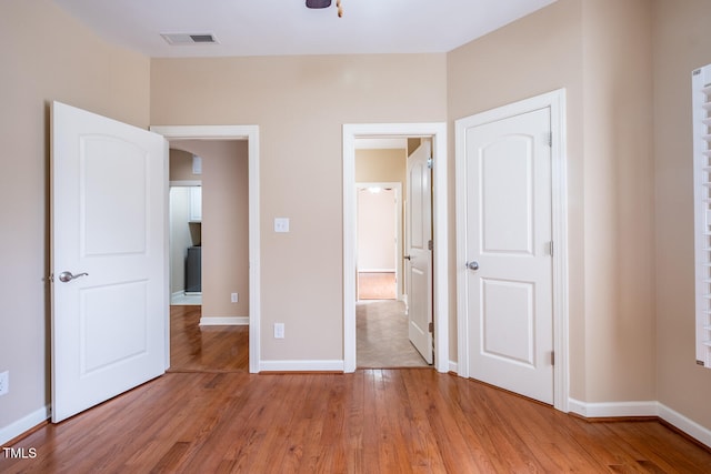 unfurnished bedroom with light wood-type flooring, visible vents, arched walkways, and baseboards