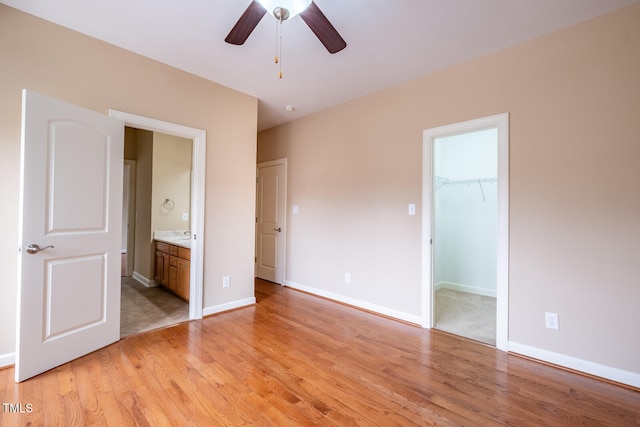 unfurnished bedroom featuring a spacious closet, connected bathroom, light wood-style flooring, and baseboards