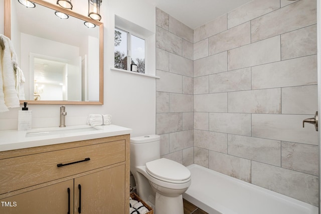 bathroom with a tile shower, vanity, and toilet