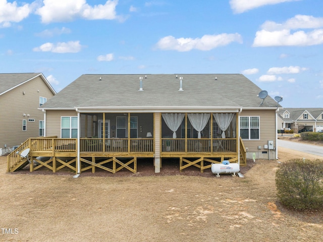 back of property with a sunroom, roof with shingles, and a deck