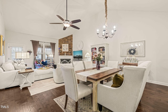 dining space with high vaulted ceiling, a chandelier, ceiling fan, dark wood finished floors, and baseboards