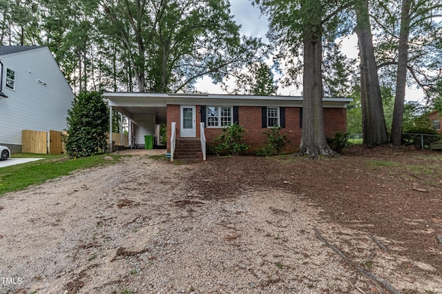 ranch-style home with a carport, driveway, brick siding, and fence