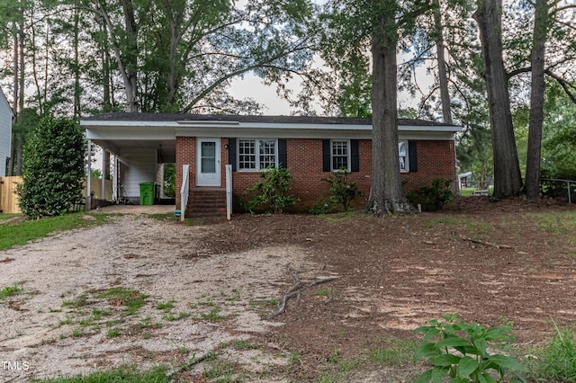 ranch-style home featuring an attached carport, brick siding, and dirt driveway