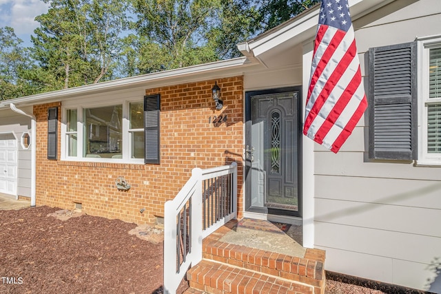 view of exterior entry with a garage, brick siding, and crawl space