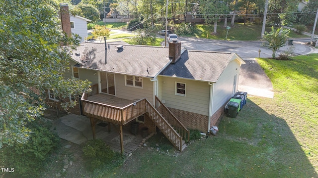 back of property featuring brick siding, a yard, a chimney, a shingled roof, and a deck